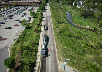 Aerial view of a construction crew using an asphalt milling machine on a road near a parking lot and green space.
